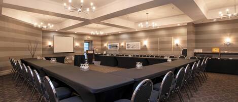 Une salle de conférence équipée d’une longue table, de chaises, d’un écran de projection et de luminaires fixés au mur.