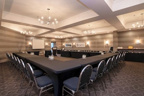 Un salón de conferencias con una larga mesa, sillas, una pantalla de proyector y luces fijadas a la pared.