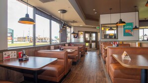 Un restaurant avec des banquettes et des tables, de grandes fenêtres et des lampes suspendues.