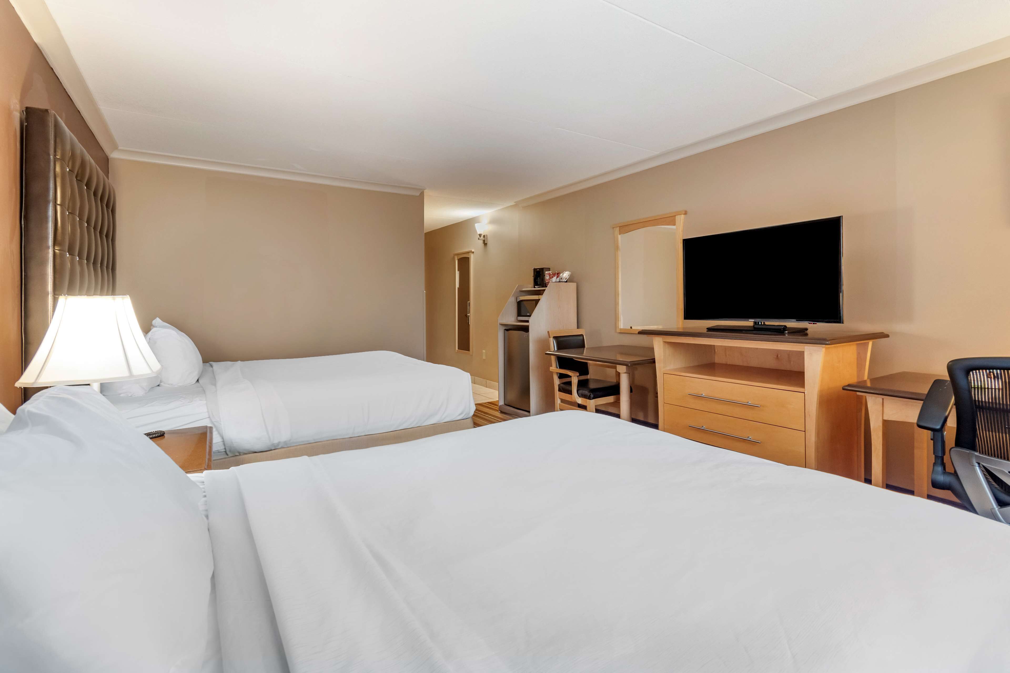 Ett hotellrum med två sängar, ett skrivbord, en stol, en tv och en spegel.