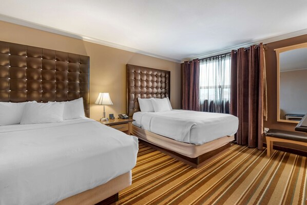 A hotel room with two beds, a large mirror, a bedside table with a lamp, and a striped carpet. - Best Western Marquis Inn & Suites (Prince Albert)