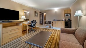 A hotel room with a flat-screen TV, a desk with a chair, a sofa, a kitchen area with a microwave, and a lamp. - Best Western Marquis Inn & Suites (Prince Albert)