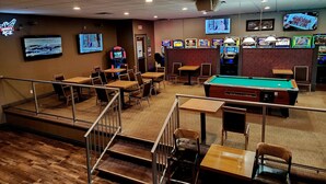 A billiards room with tables, chairs, a pool table, arcade games, and multiple screens. - Best Western Marquis Inn & Suites (Prince Albert)