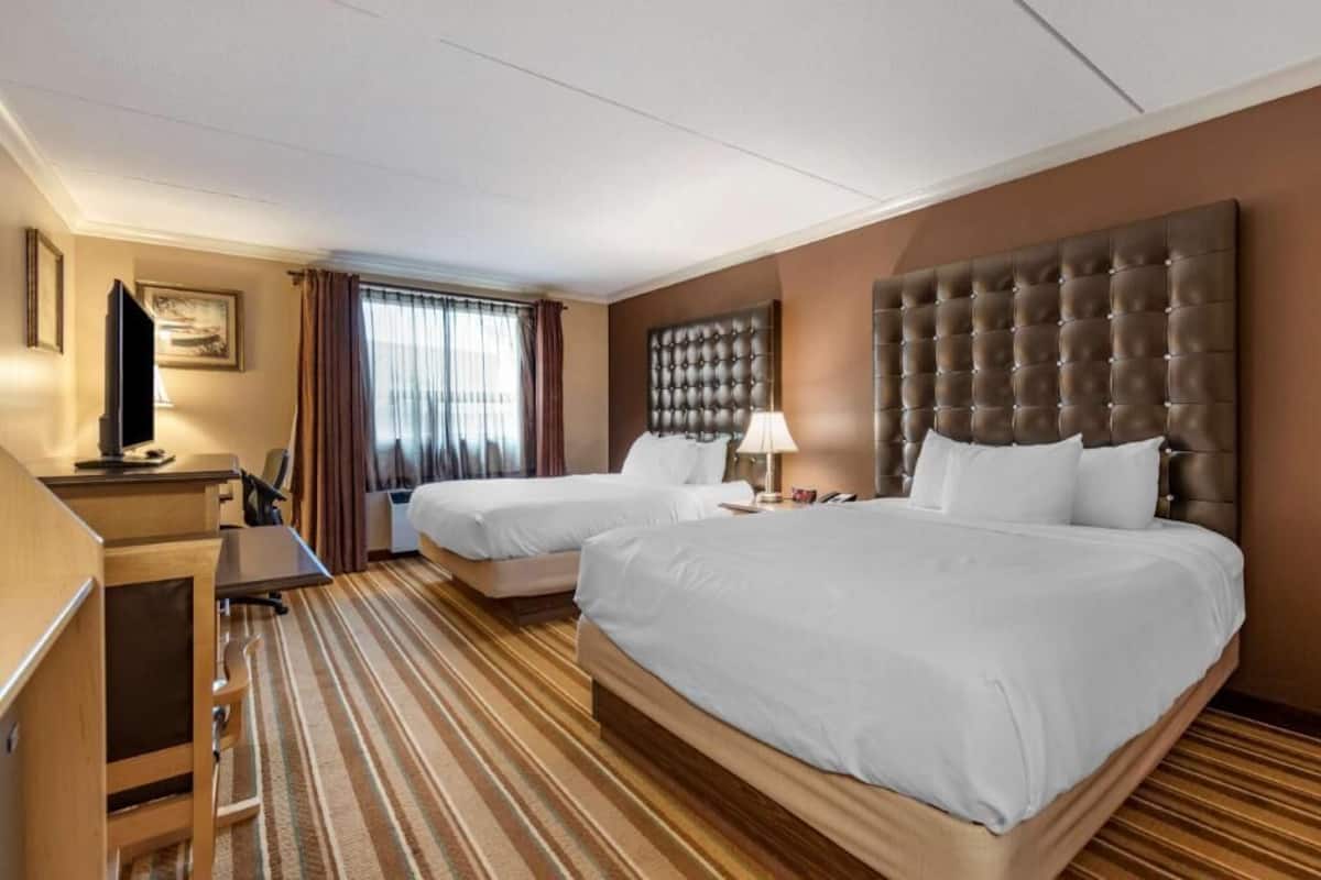 A hotel room with two beds, a desk, a television, and a large window with curtains.