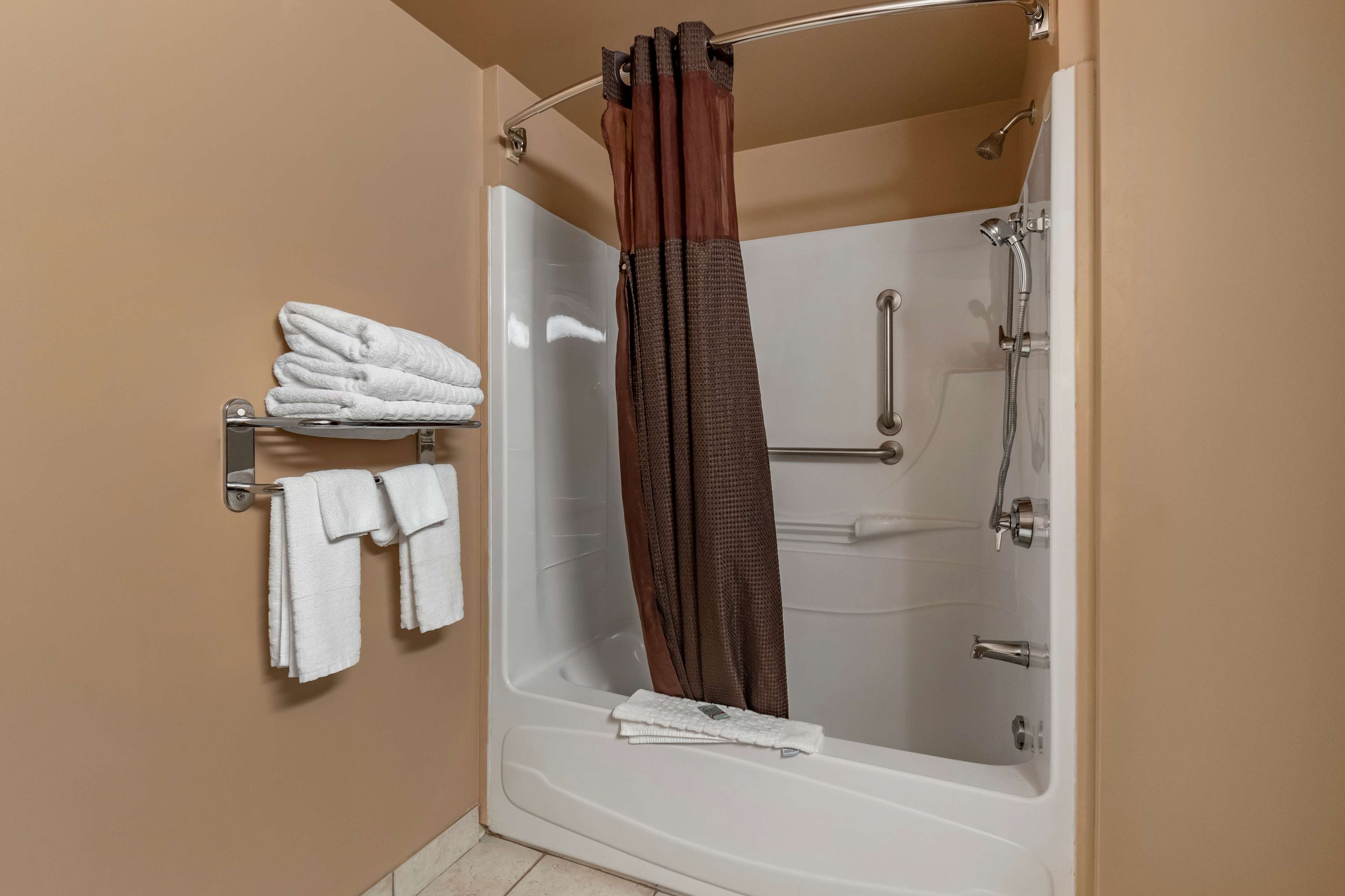 A walk-in shower with a glass door, a towel rack with folded towels, and a shower curtain.