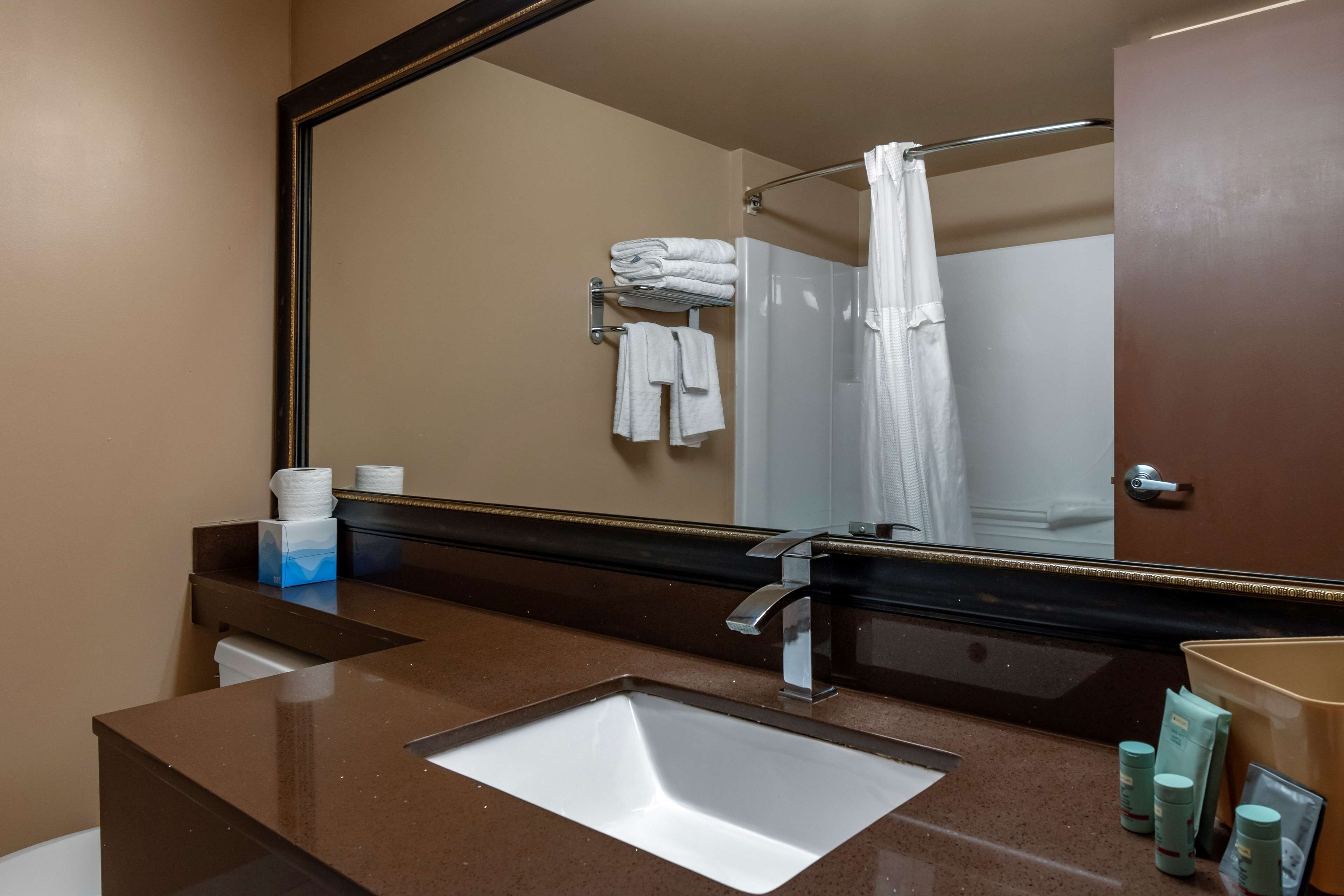 Un baño con lavamanos, espejo, toallero y artículos de aseo.