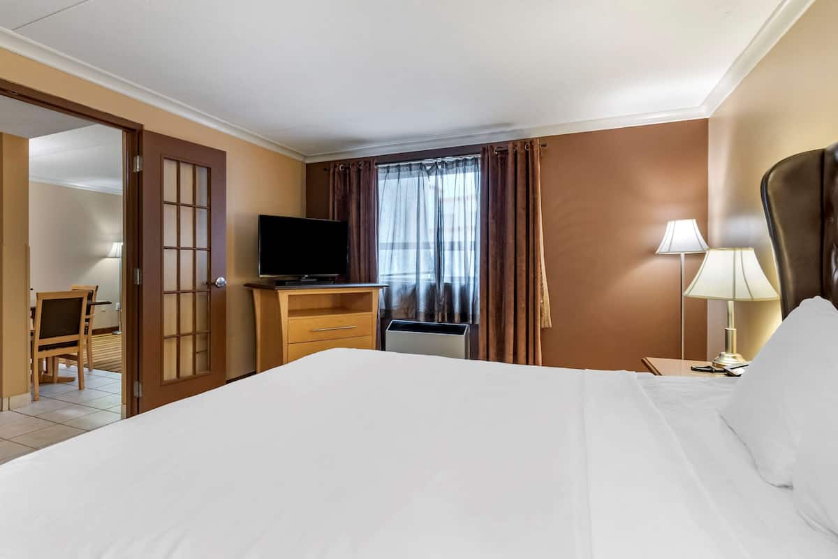 A hotel room with a bed, a TV, a desk, a chair, and a window with curtains.