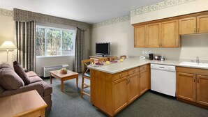 Un espacio habitable compacto con kitchenette, comedor y zona de estar con sofá y mesa.