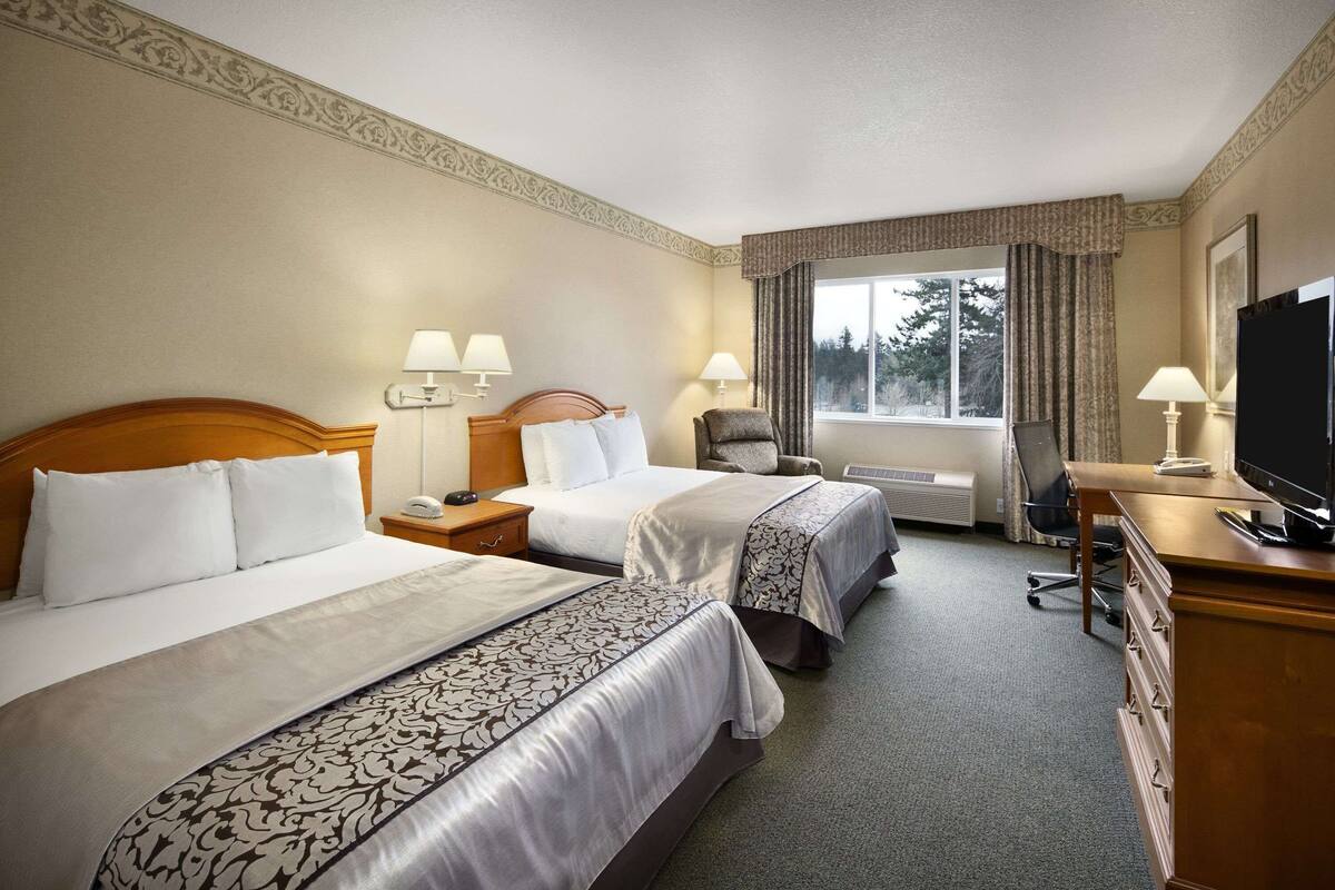 Une chambre d’hôtel avec deux lits, un bureau avec une télévision et une fenêtre avec des rideaux.