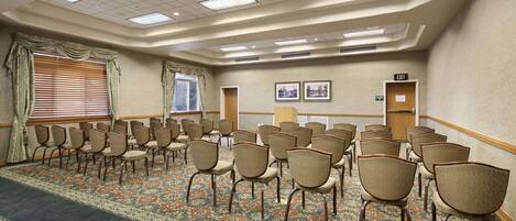 Un salón de conferencias con filas de sillas, suelo alfombrado e iluminación empotrada en el techo.