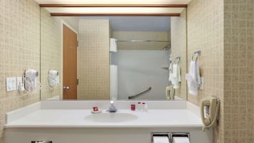A bathroom with a large mirror, a sink, a shower, and a telephone.