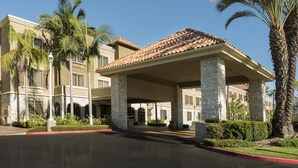 A hotel with a covered entrance, stone columns, and palm trees.