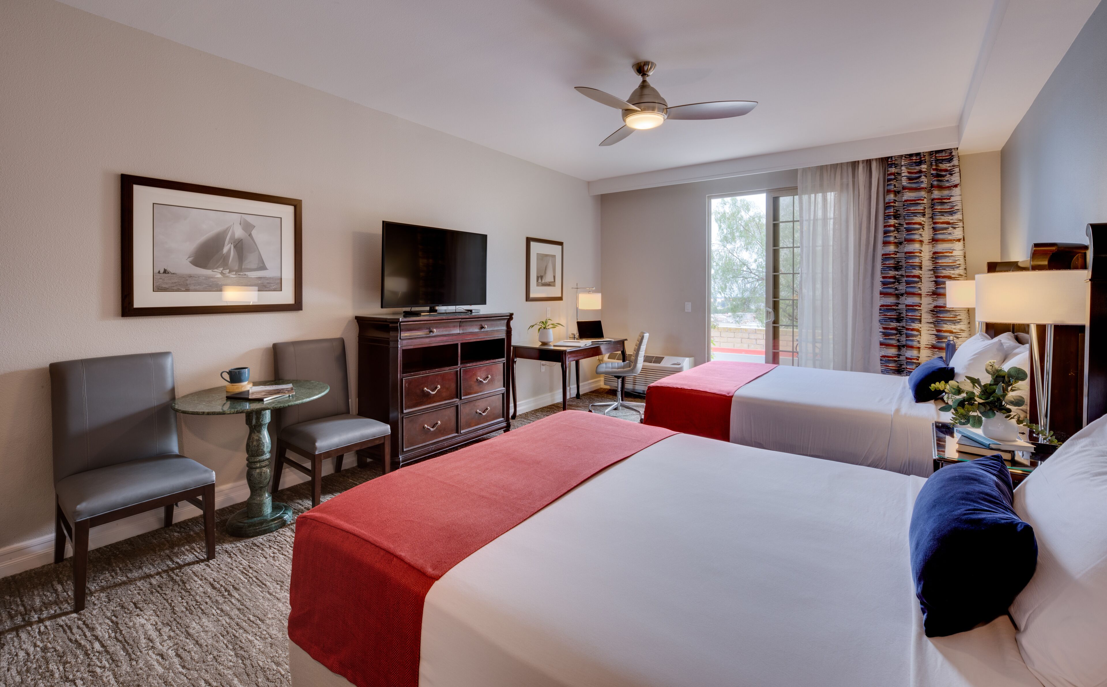 A hotel room with two beds, a desk with a computer, a television, a chair, and a small table.