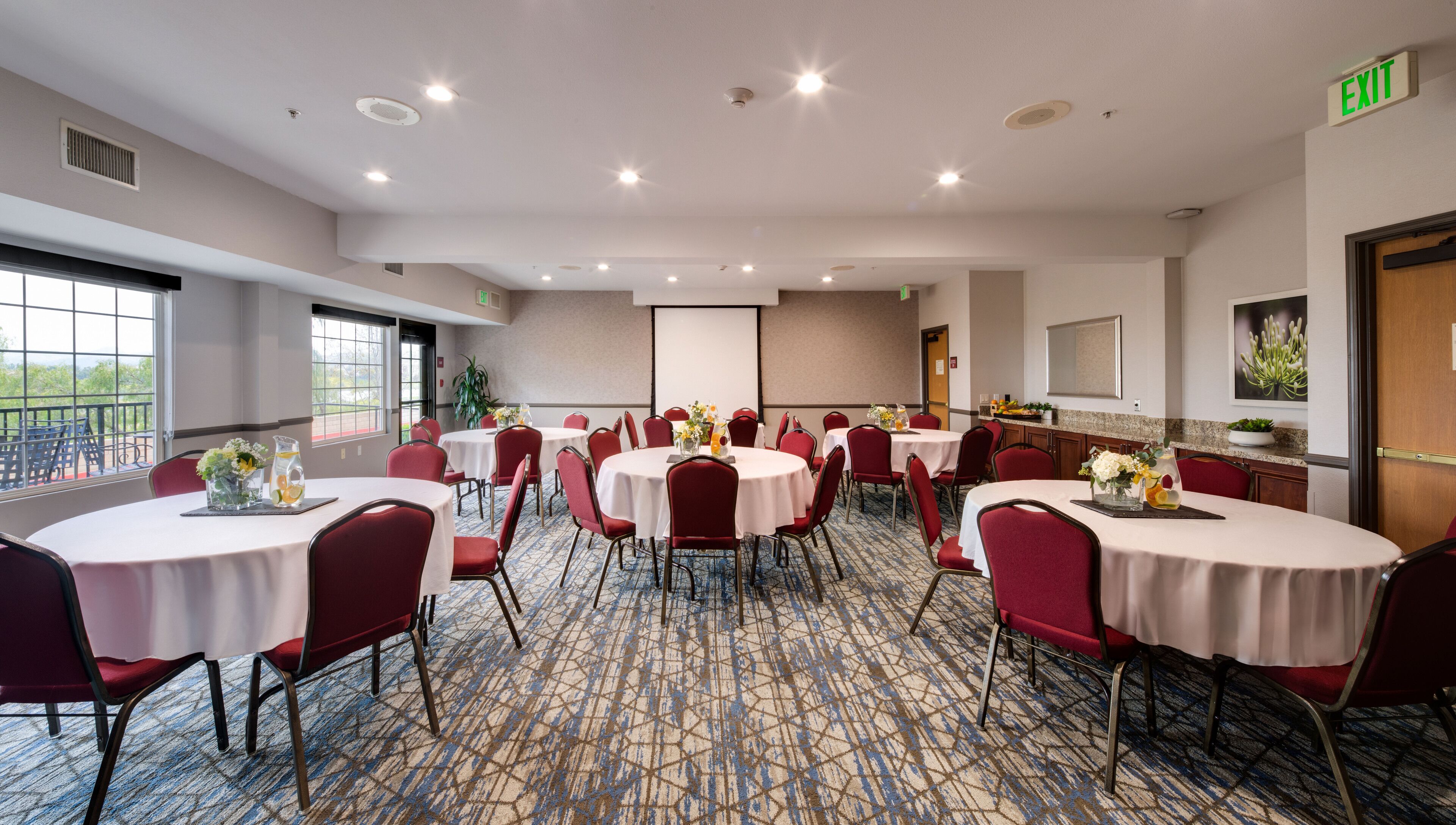 A conference room with round tables, red chairs, and a projector screen.
