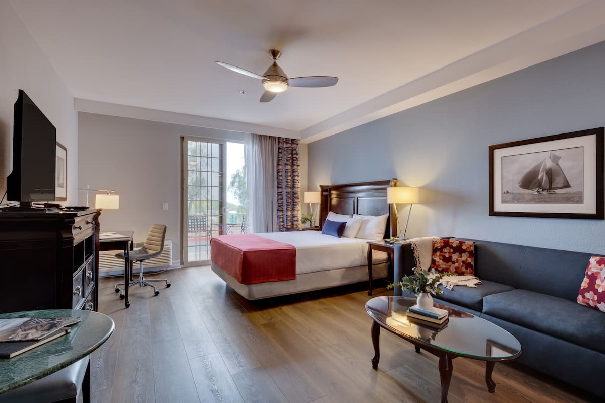 Een hotelkamer met een bed, een bank, een bureau, een televisie en een plafondventilator.