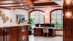 A reception area with a wooden counter, a desk with two chairs, a large arched window, and a stone wall.