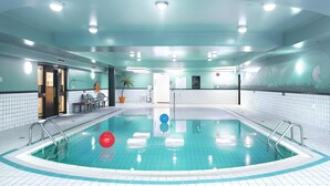 An indoor swimming pool with clear water, tiled walls, and ceiling lights.
