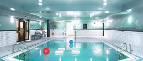 En indendørs swimmingpool med krystalklart vand, flisebeklædte vægge og loftslamper.