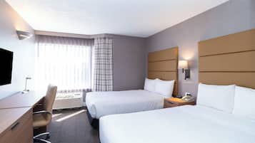 A hotel room with two beds, a desk, a chair, and a TV.