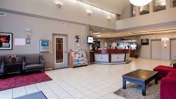 A hotel lobby with a reception desk, seating area, and a bulletin board.
