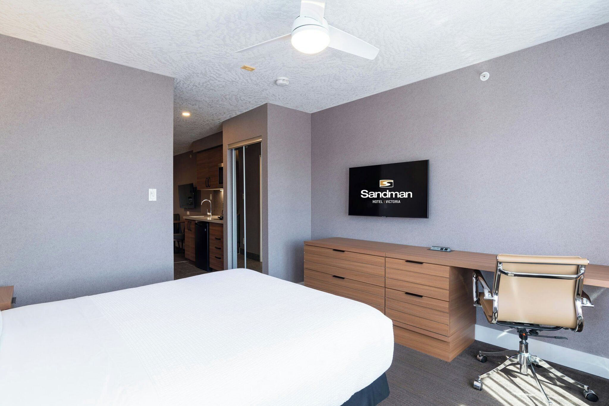 A hotel room with a bed, a desk with a chair, a television, and a ceiling fan.