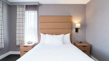 Une chambre d’hôtel avec un grand lit, une table de chevet avec une lampe, un téléphone et une petite table de nuit avec une horloge.