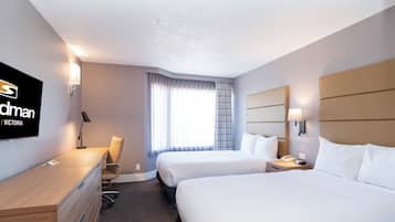 A hotel room with two beds, a desk, a chair, a TV, and a window with curtains.