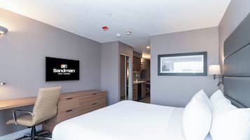 Habitación de hotel con cama, escritorio, silla, televisión y baño visible a través de una puerta abierta.