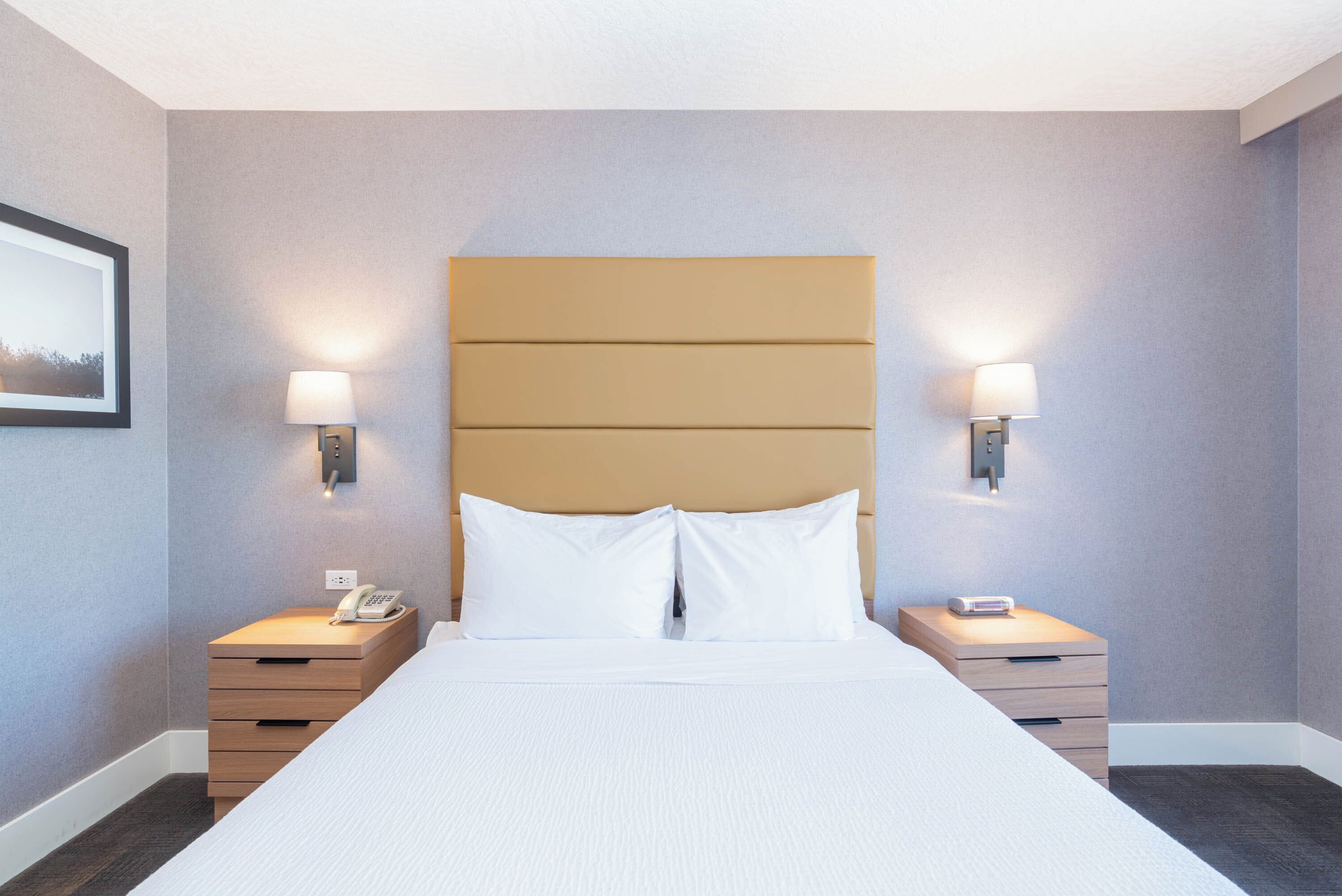 A hotel room with a large bed, two bedside tables, a wall-mounted phone, and two wall-mounted lamps.