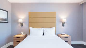 A hotel room with a large bed, two bedside tables, a wall-mounted phone, and two wall-mounted lamps.