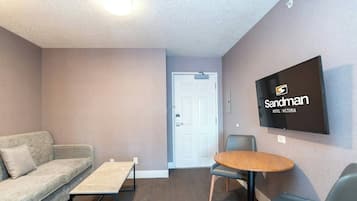 A hotel room with a sofa, a small table, a round wooden table, and a TV mounted on the wall.