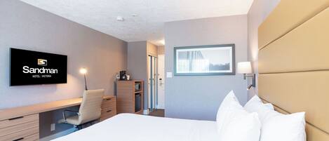 A hotel room with a bed, a desk, a chair, a TV, and a window.