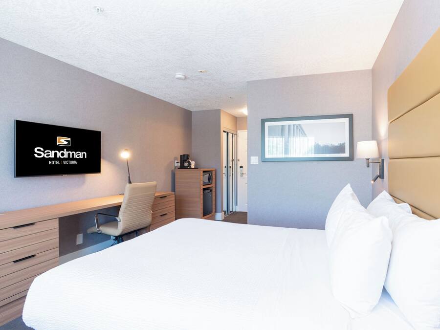 A hotel room with a bed, a desk, a chair, a TV, and a window.