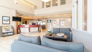A spacious lobby with grey sofas, a reception desk, and a digital information board.