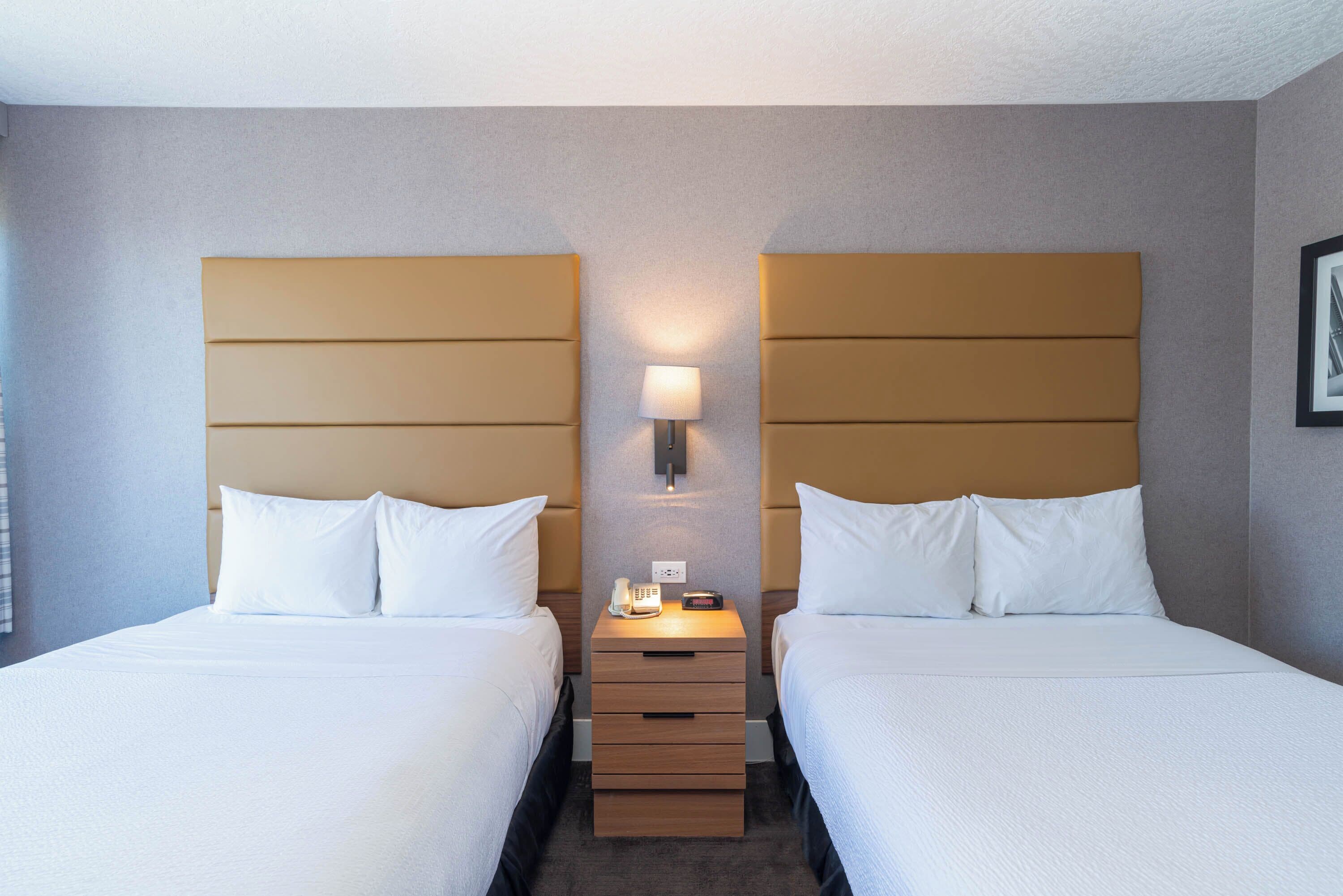 Une chambre d’hôtel avec deux lits, une table de chevet avec une lampe et un téléphone fixé au mur.