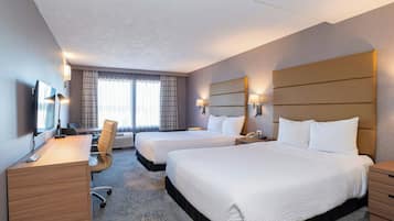 A hotel room with two beds, a desk, a chair, a TV, and a window with curtains.