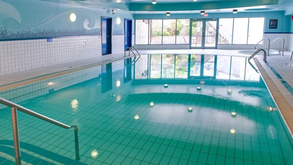 Una piscina interior con agua cristalina, paredes de azulejos y ventanas que dejan pasar la luz natural.