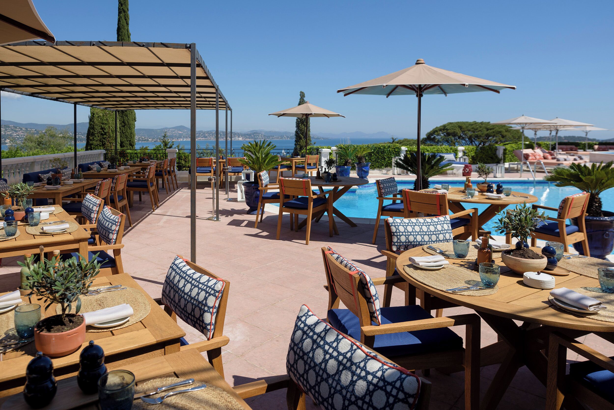 An outdoor dining area with tables and chairs, a pool, and umbrellas.