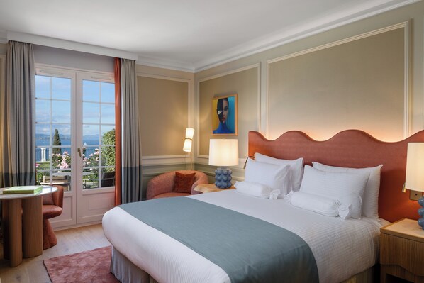 A hotel room with a large bed, a desk, a chair, and a view of the outdoors. - Althoff Hotel Villa Belrose (Gassin)