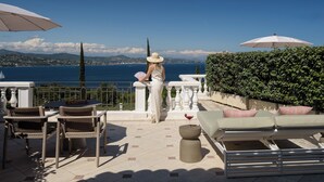 A terrace with outdoor furniture, a view of the sea, and a person reading a book. - Althoff Hotel Villa Belrose (Gassin)