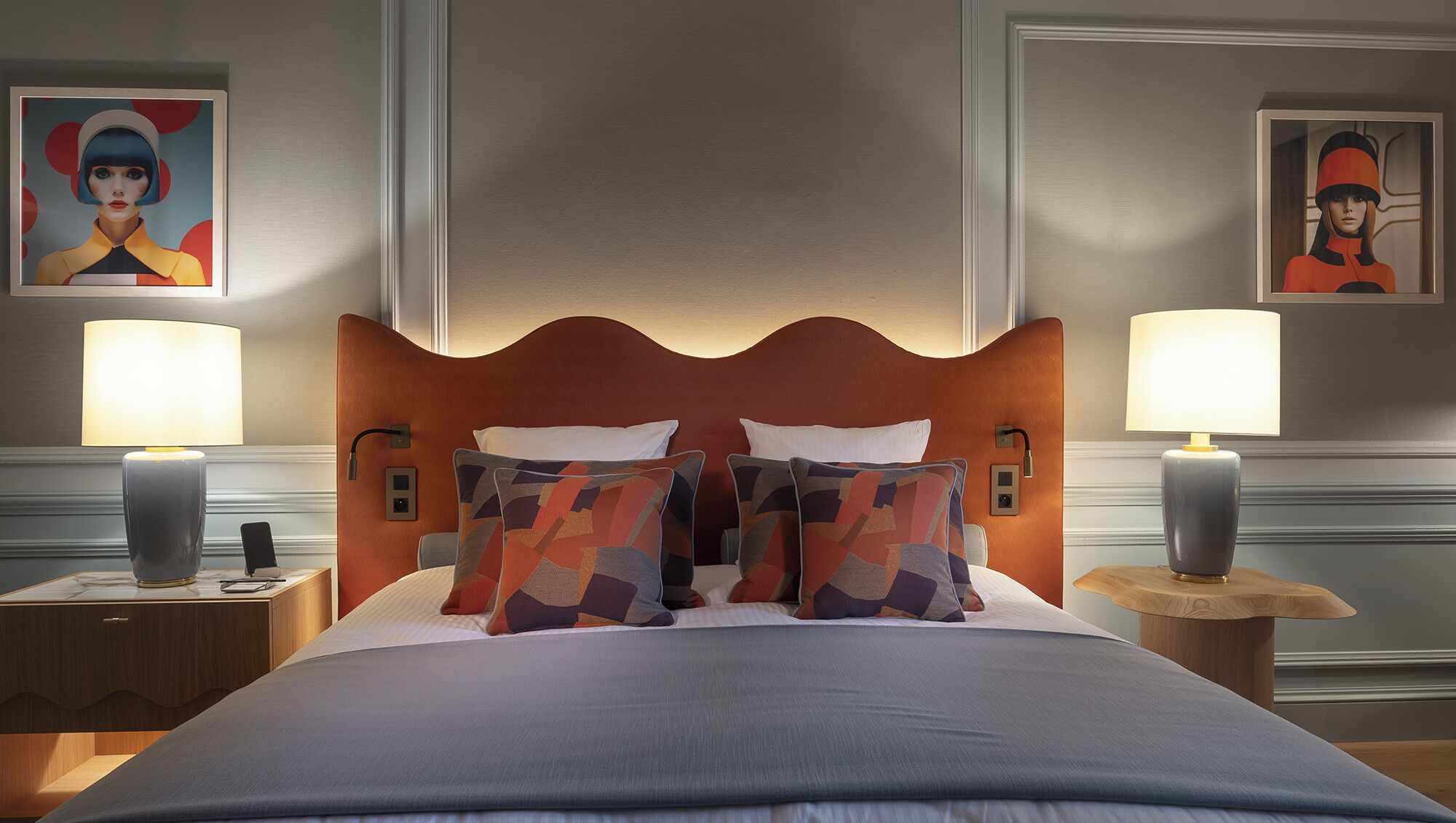 Une chambre d’hôtel avec un grand lit, deux tables de chevet avec des lampes et deux tableaux accrochés au mur.
