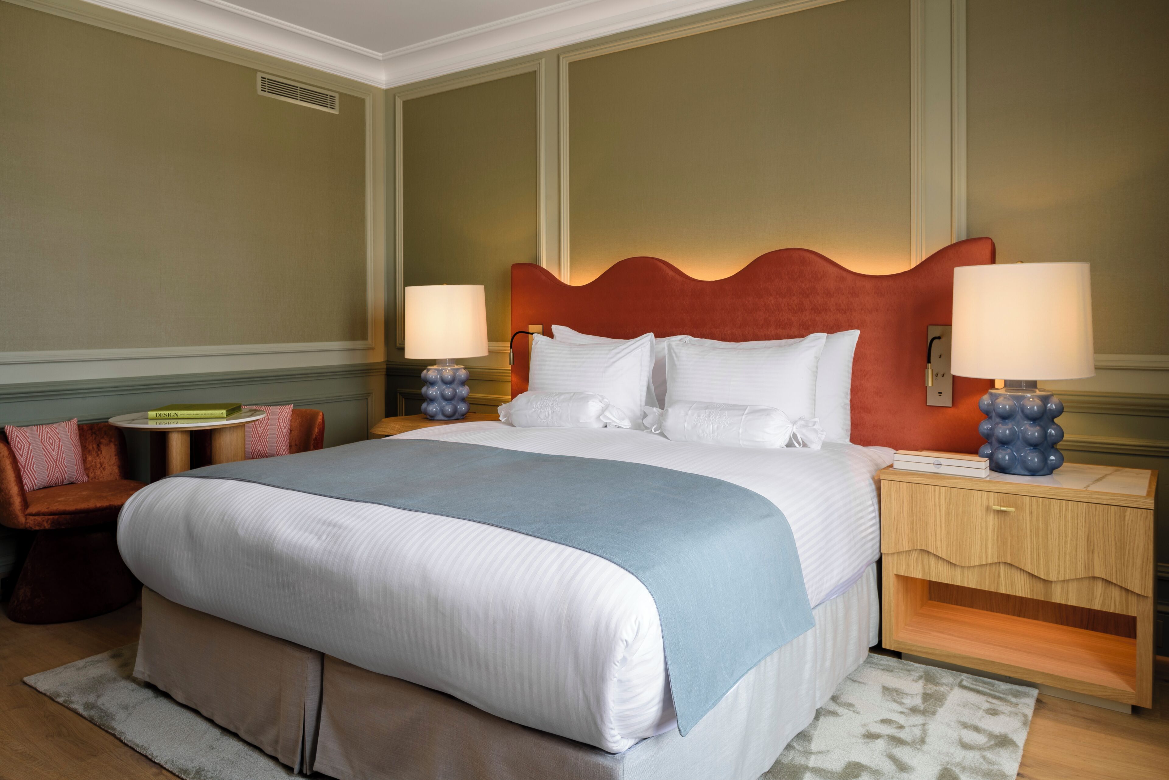 A hotel room with a large bed, two bedside tables, a nightstand, a chair, and a rug.
