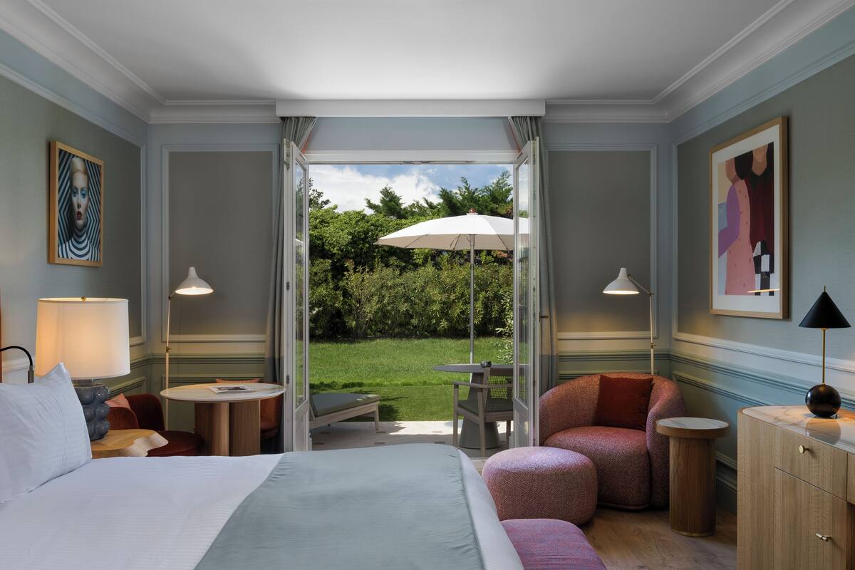 A hotel room with a bed, a desk, a chair, a small table, and an umbrella outside.