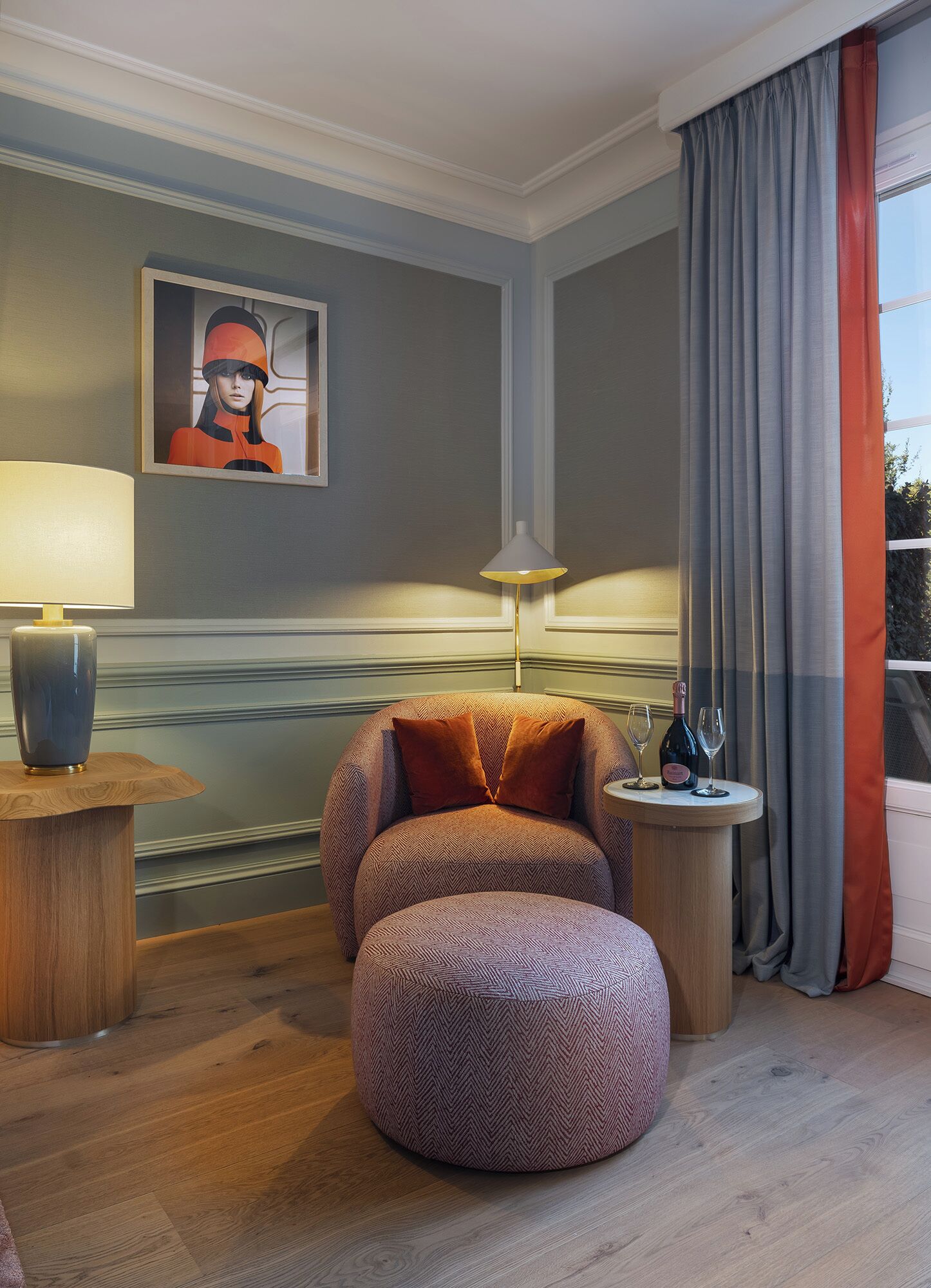 Ein gemütliches Zimmer mit einem runden Sessel, einem kleinen Hocker, einer Lampe und einem Tisch mit Flasche und Glas.
