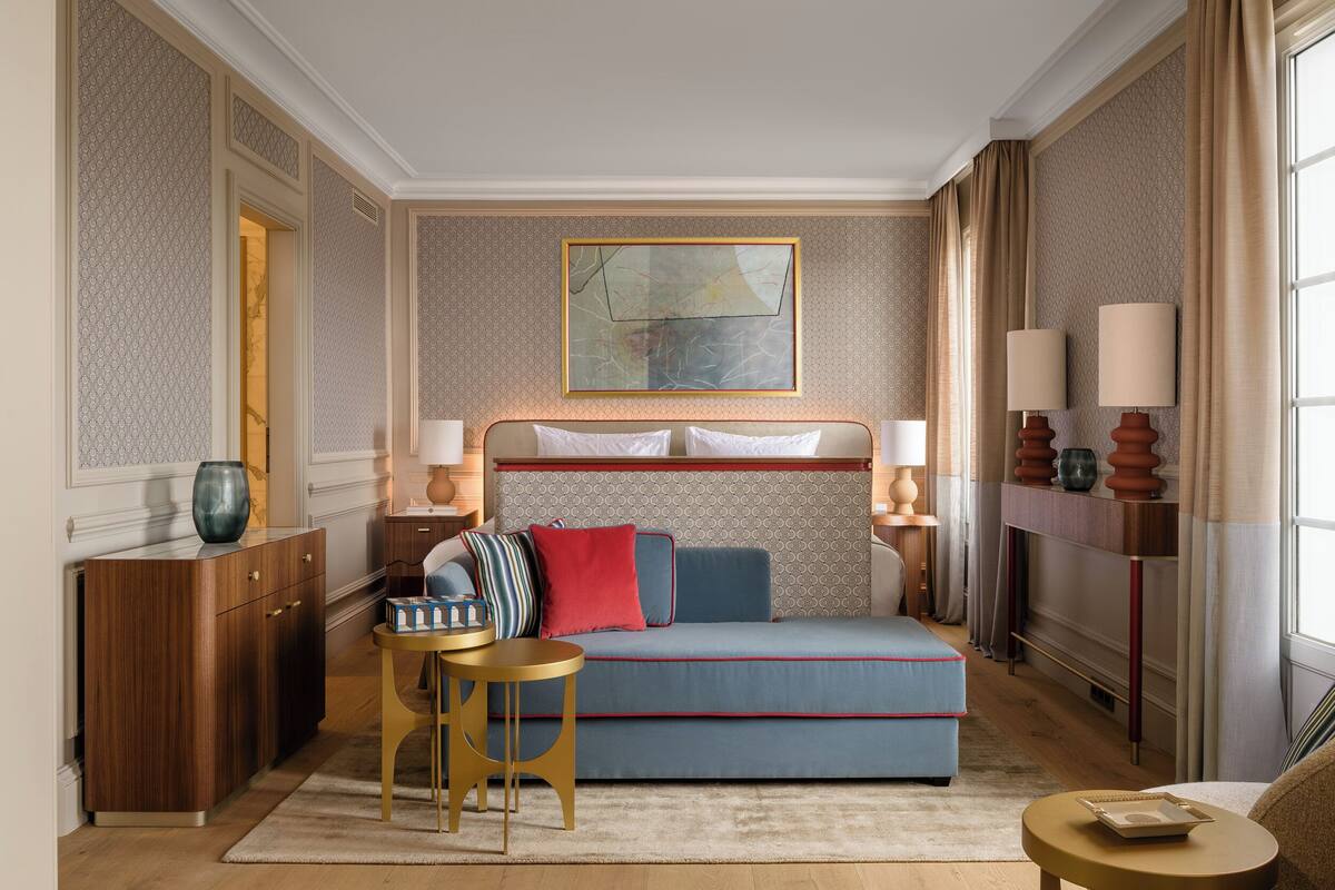 A hotel room with a bed, a sofa, a small table, a cabinet, and a painting on the wall.