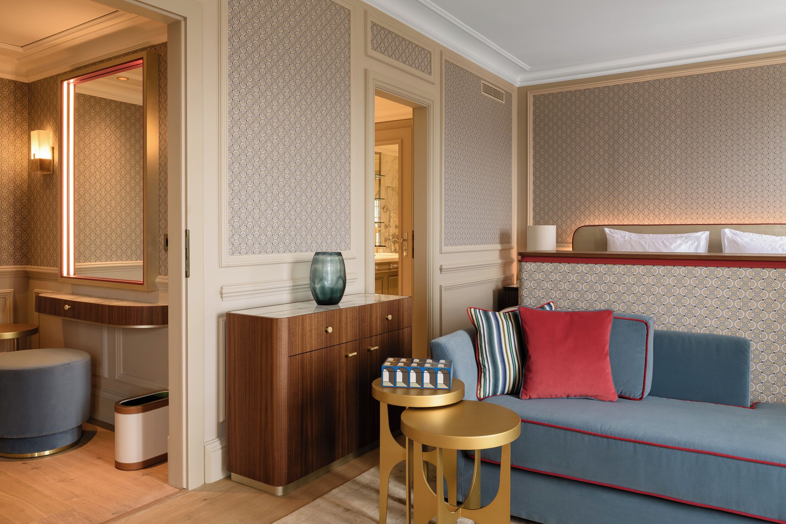 A hotel room with a wooden cabinet, a blue sofa with red cushions, a small round table, and a mirror.