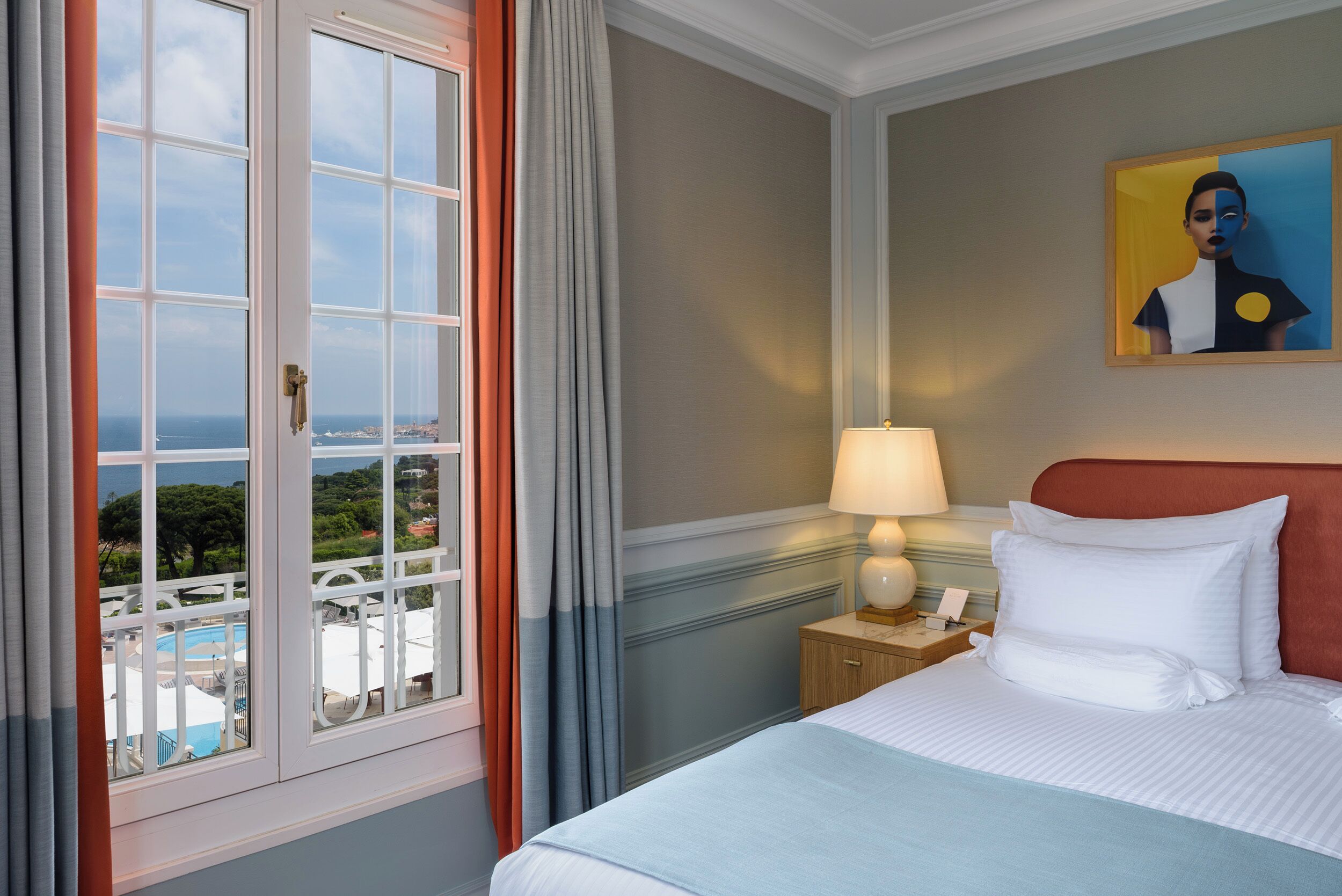 A hotel room with a bed, a nightstand, a lamp, a painting, and a window with curtains.