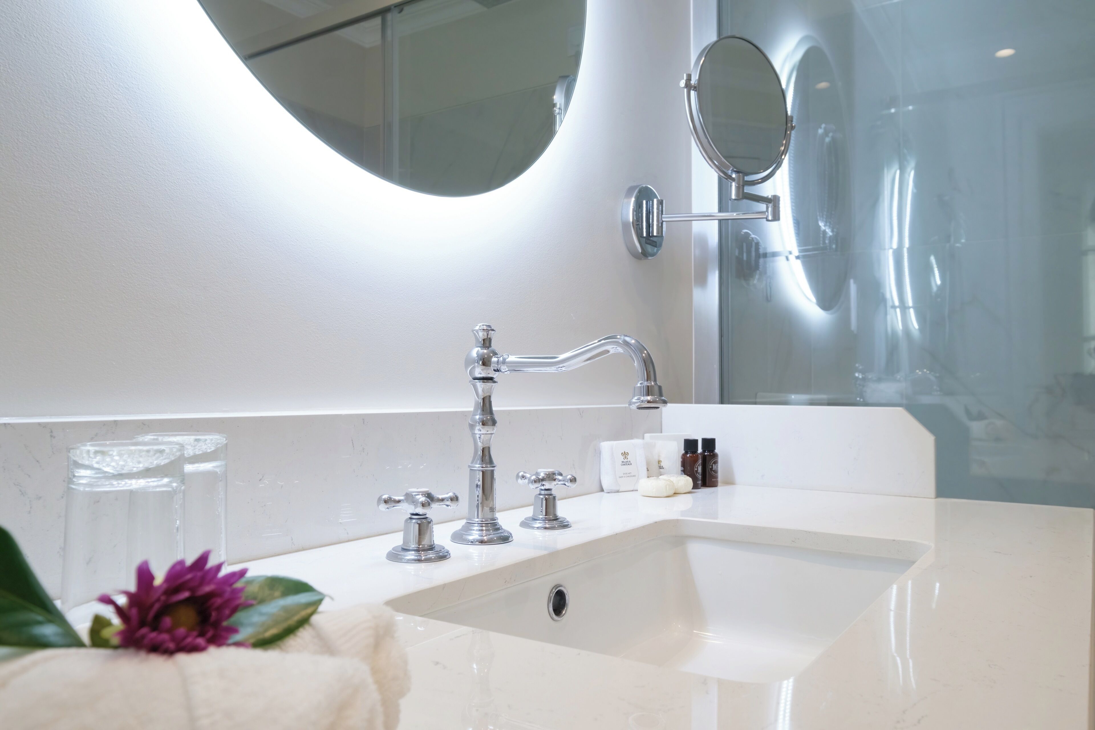 A bathroom with a white sink, two faucets, a mirror, and a glass shower enclosure.