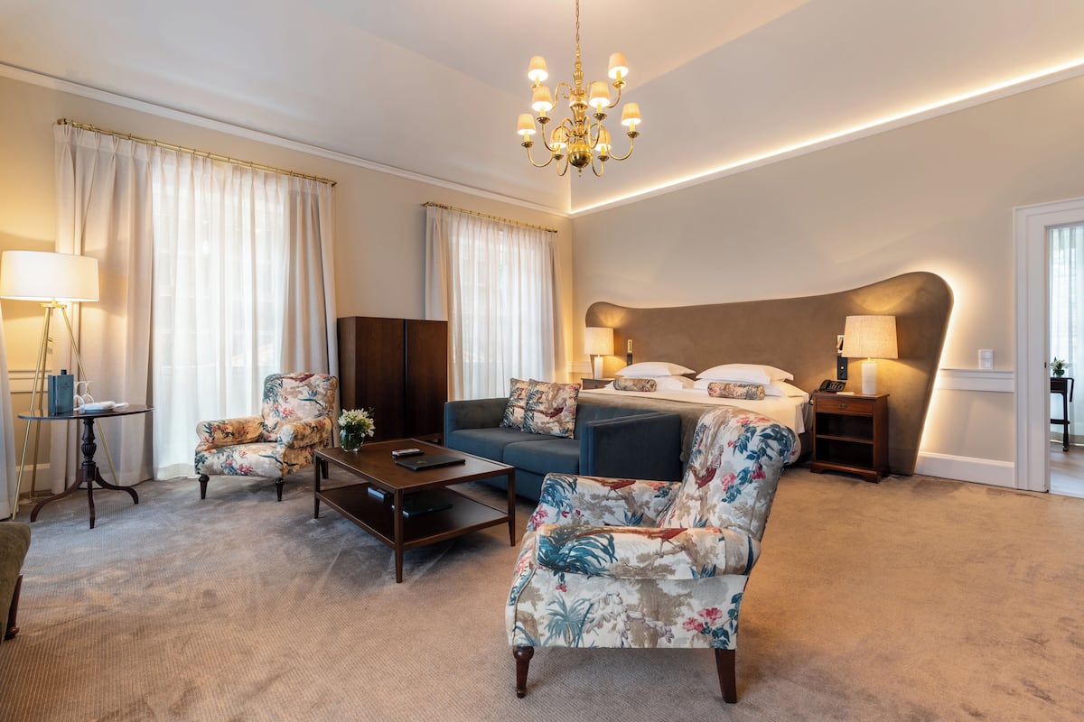 Una habitación de hotel amplia con una cama grande, un sofá, una silla, una mesita de café y un escritorio.