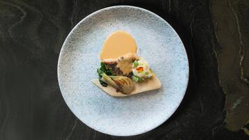 Un plato con un trozo de carne, vegetales verdes y una cucharada de salsa sobre un plato azul con textura.